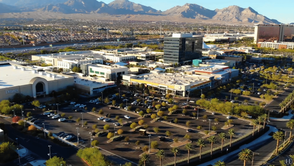 Aerial view of Las Vegas commercial shopping center with Dillard’s department store, office buildings, parking lots, palm trees, and mountain backdrop